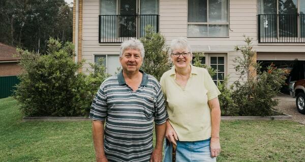 Older couple smiling in front of house