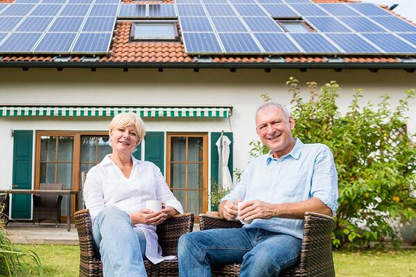 A senior couple sitting in their yard in front of their house with solar panels on the roof