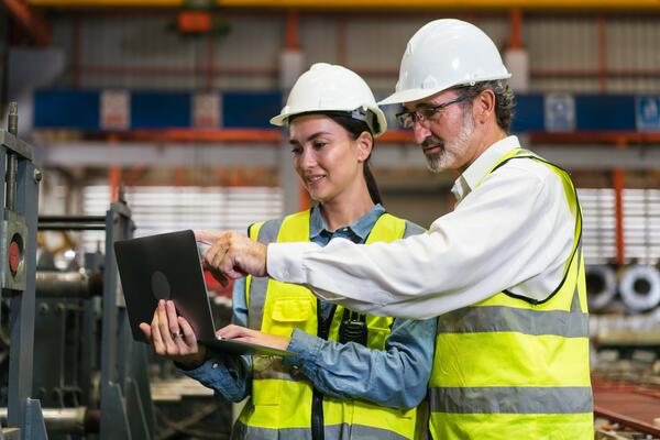 Two workers inside a factory wearing PPE looking at a tablet