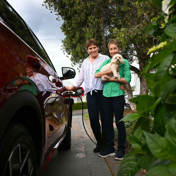 Smiling couple charging electric vehicle, holding dog 